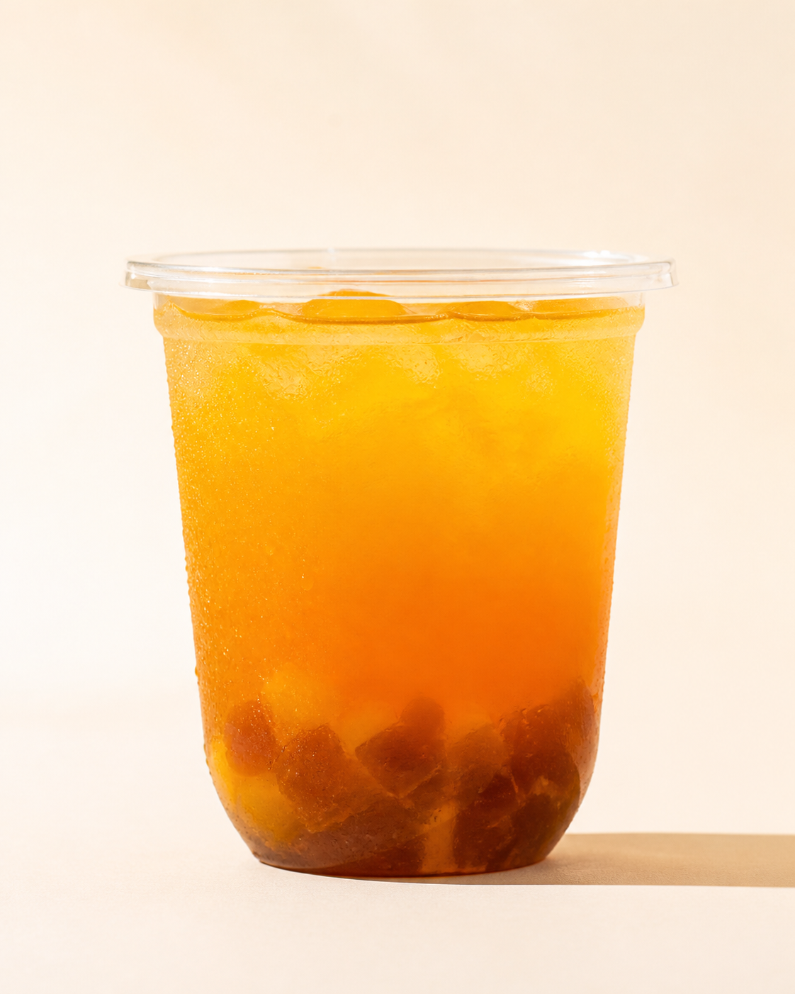 Breiter Becher goldener Mango Tea mit dunklen Mango-Jelly-Stücken am Boden.