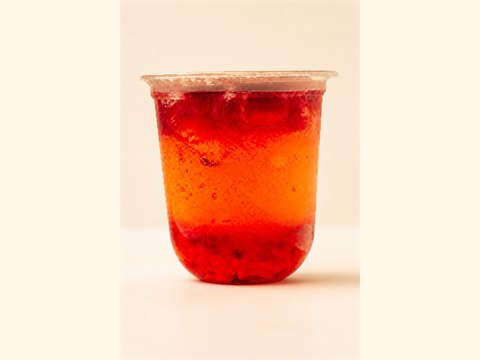 Wide cup of translucent strawberry fruit tea with vivid red fruit layers.